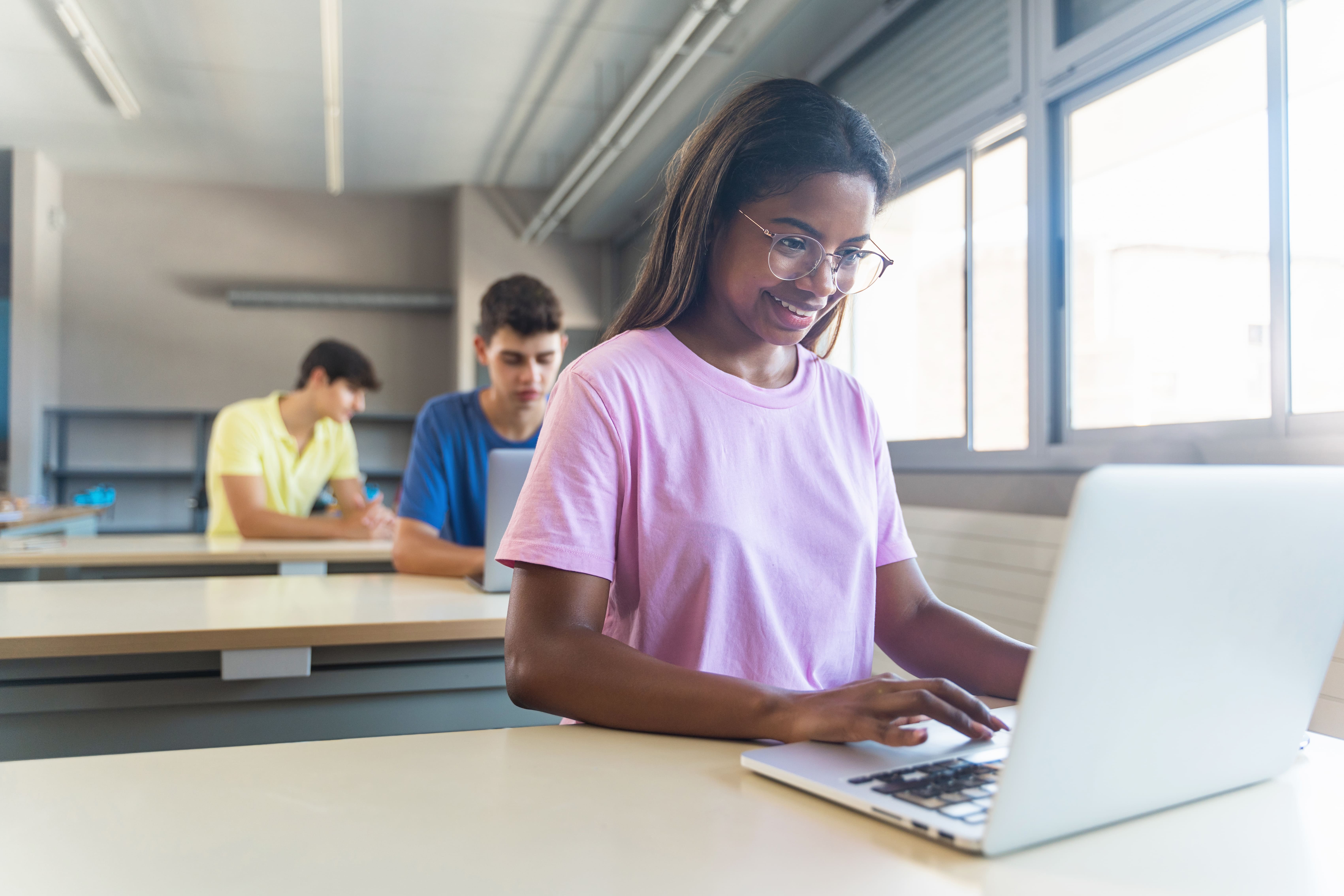 A group of diverse children collaborating on a digital project around a laptop in a modern classroom